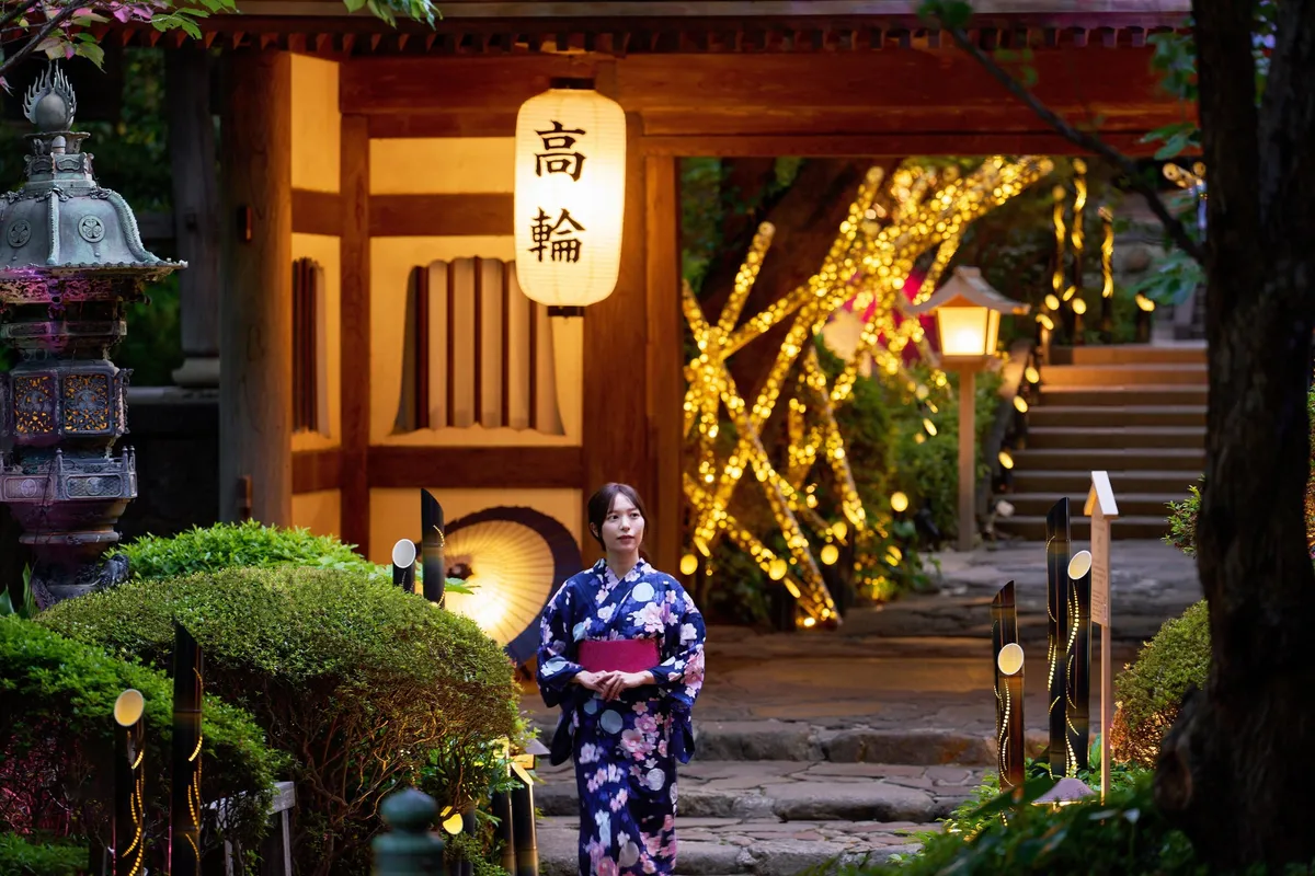 Woman in blue yukata walking through an illuminated garden gate