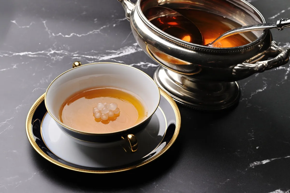 Beef consommé being poured into a gold-rimmed cup