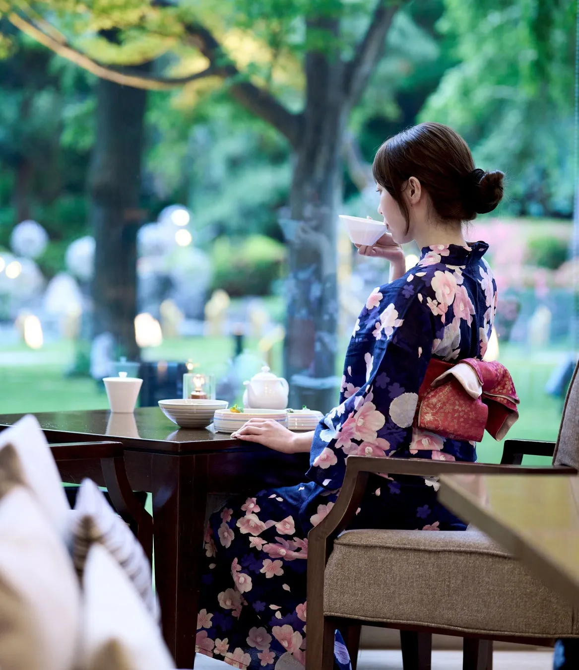 Guest in yukata enjoying tea overlooking the illuminated garden