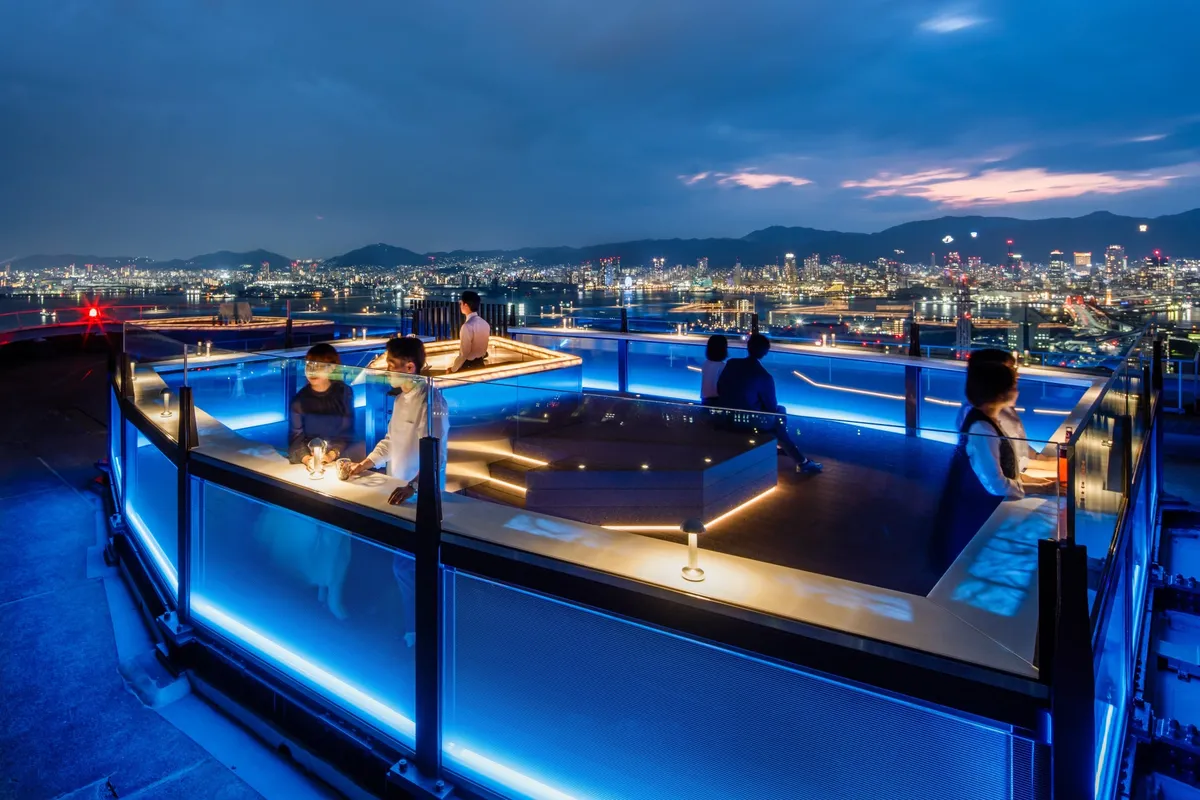 People enjoying the Sora-fune Kobe rooftop terrace with blue accent lighting