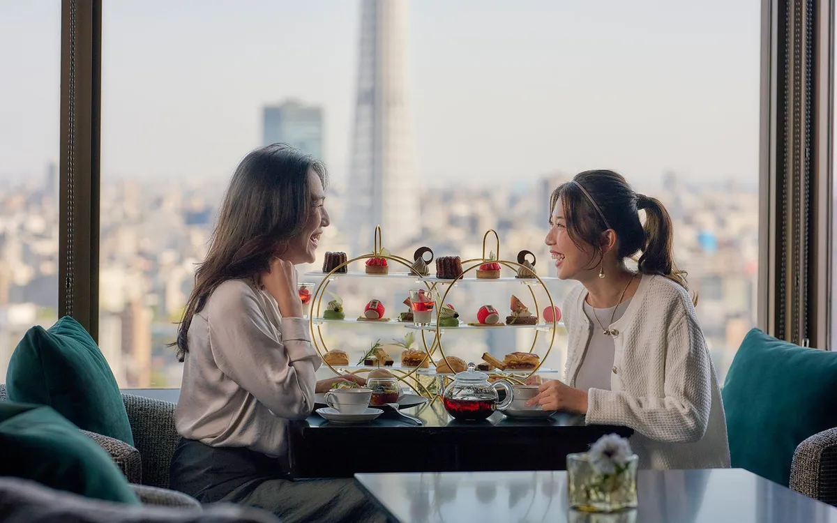 Two guests enjoying tea and sweets with the Tokyo Skytree in the background.