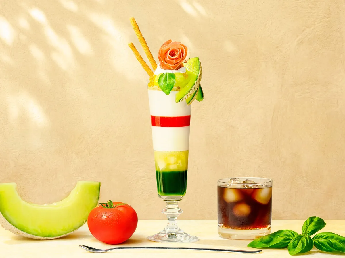 A tall glass parfait topped with a prosciutto rose and fresh melon slices