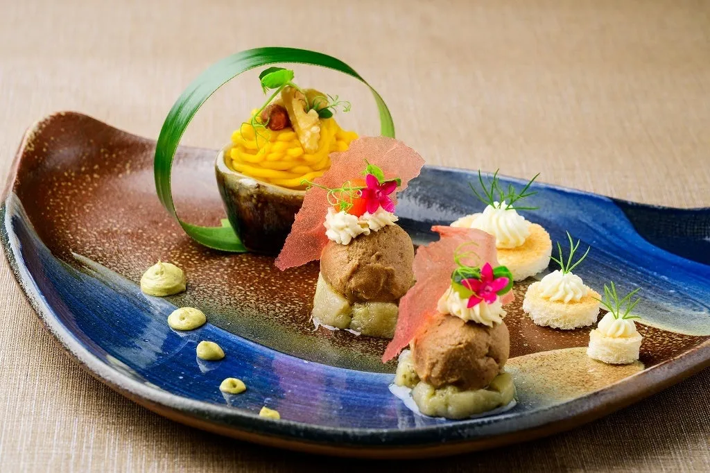Foie gras and pumpkin montblanc on a curved blue and brown ceramic plate.