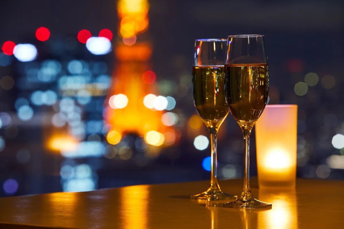 Two champagne glasses on a table with a blurred night view of Tokyo Tower
