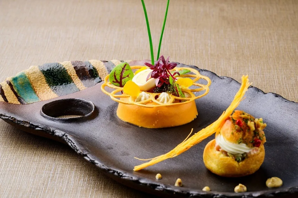 An appetizer featuring delicate garnishes on a dark, textured ceramic platter.