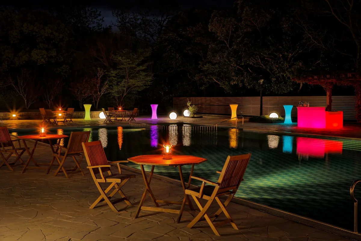 The illuminated poolside area with colorful light pillars and dining tables
