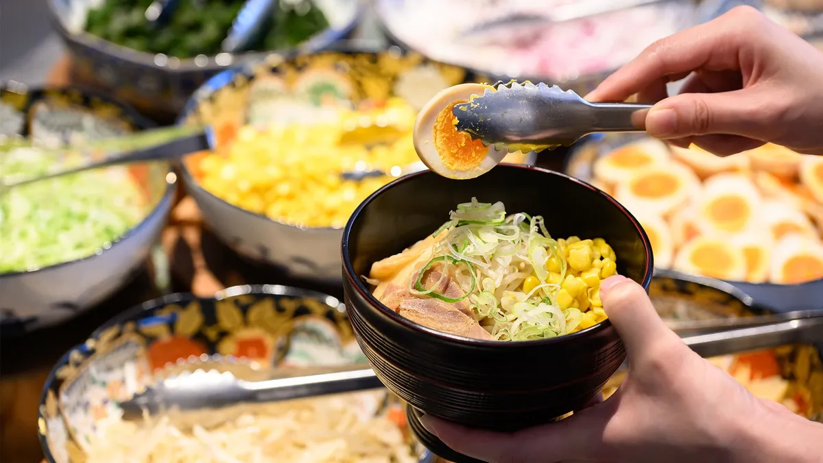 A bowl of ramen being topped with corn and egg