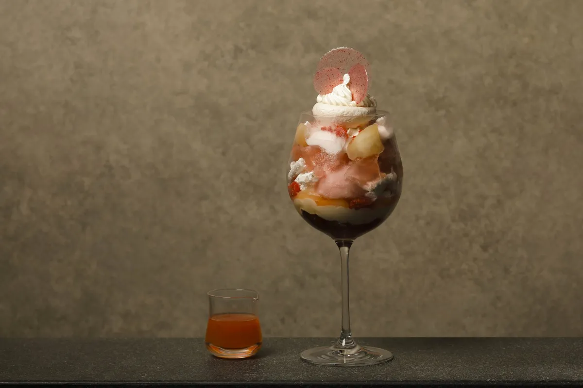 A tall, layered peach parfait served with grapefruit sauce
