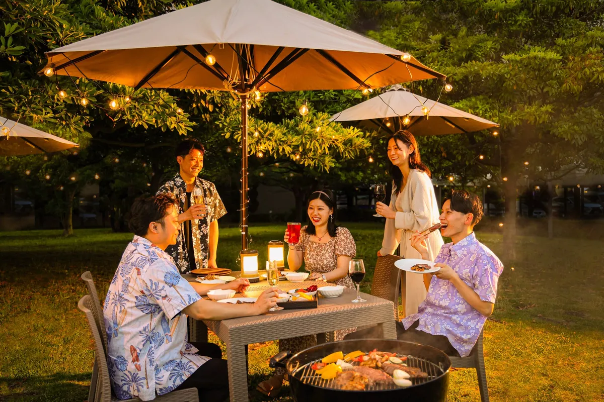 Guests dining at tables with umbrellas in a garden illuminated by string lights