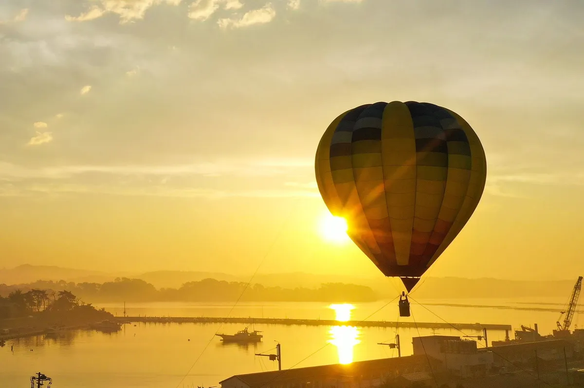 A hot air balloon rising over the water at sunrise.