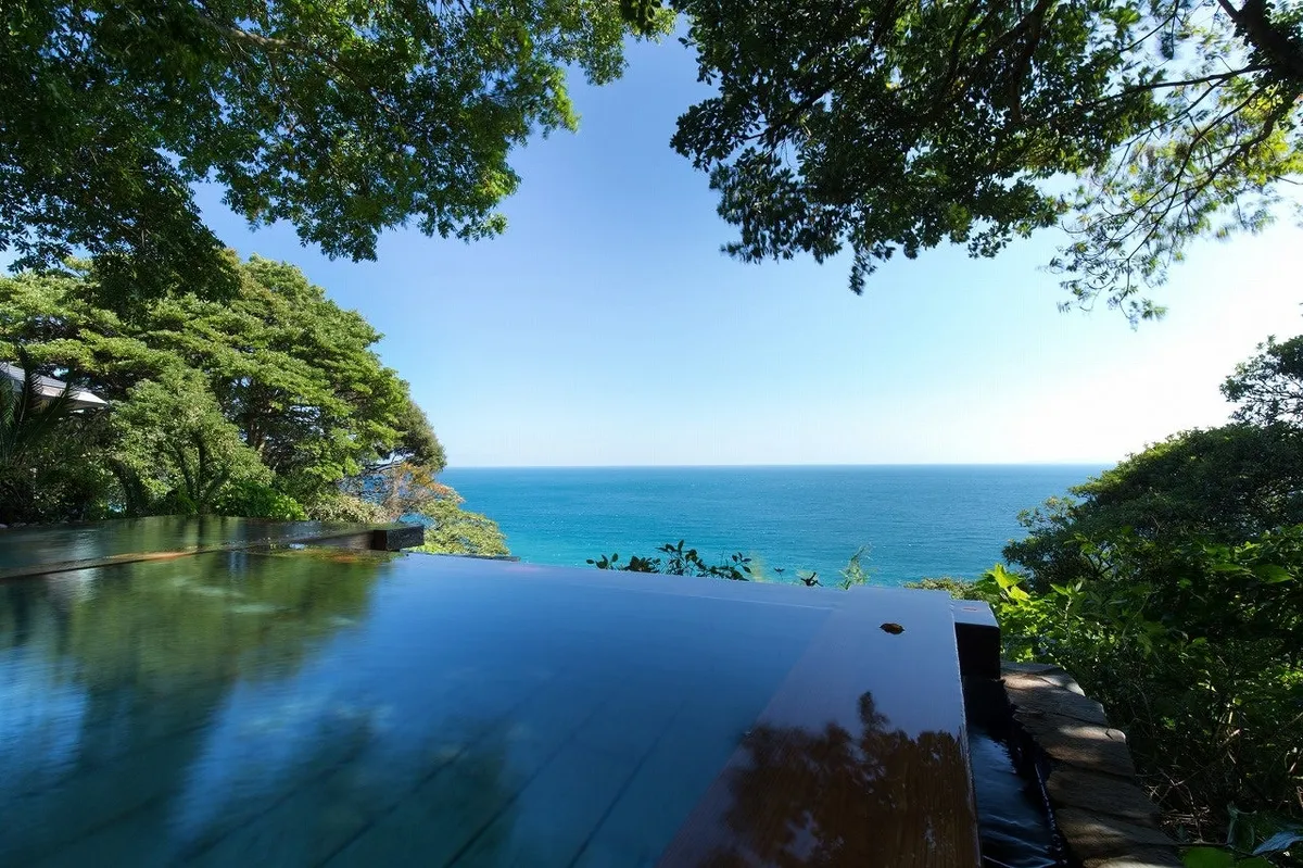 An outdoor infinity-style hot spring bath with a wooden rim overlooking the ocean.