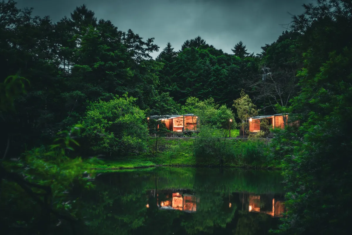 Earthboat cabins illuminated at night by the pond