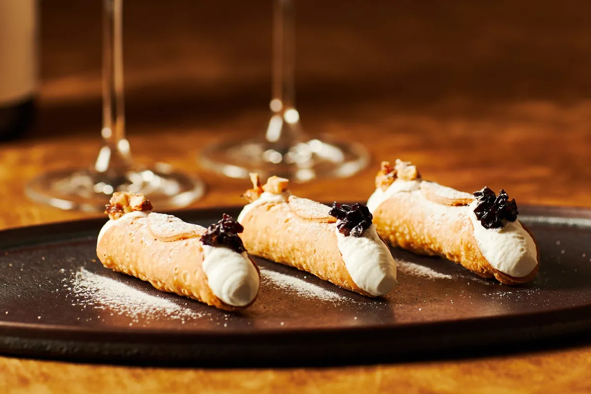 Three cannoli topped with walnuts and dried wine grapes