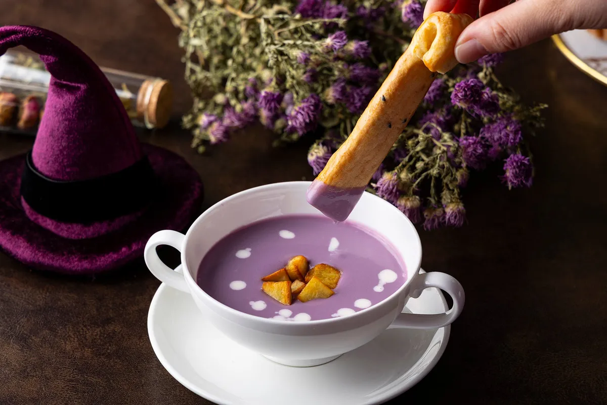Scone being dipped into purple yam soup
